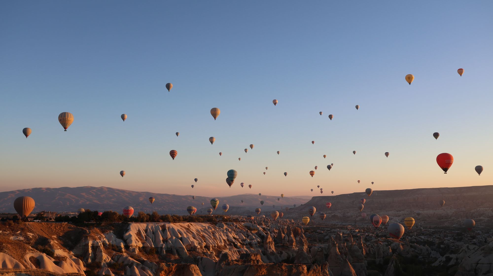 Kapadokya'da gün doğumunda peribacalarının üzerinde süzülen sıcak hava balonları